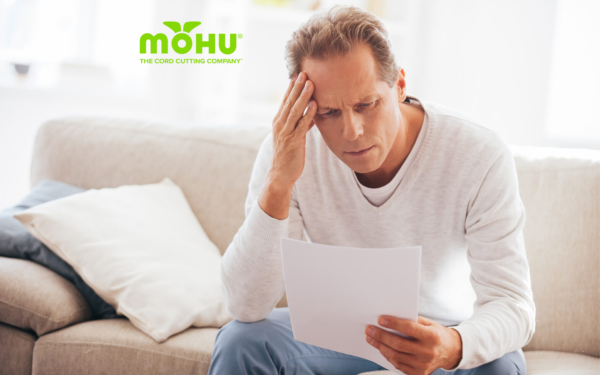 Man looking at bill sitting on couch with hand on his head and Mohu logo on top